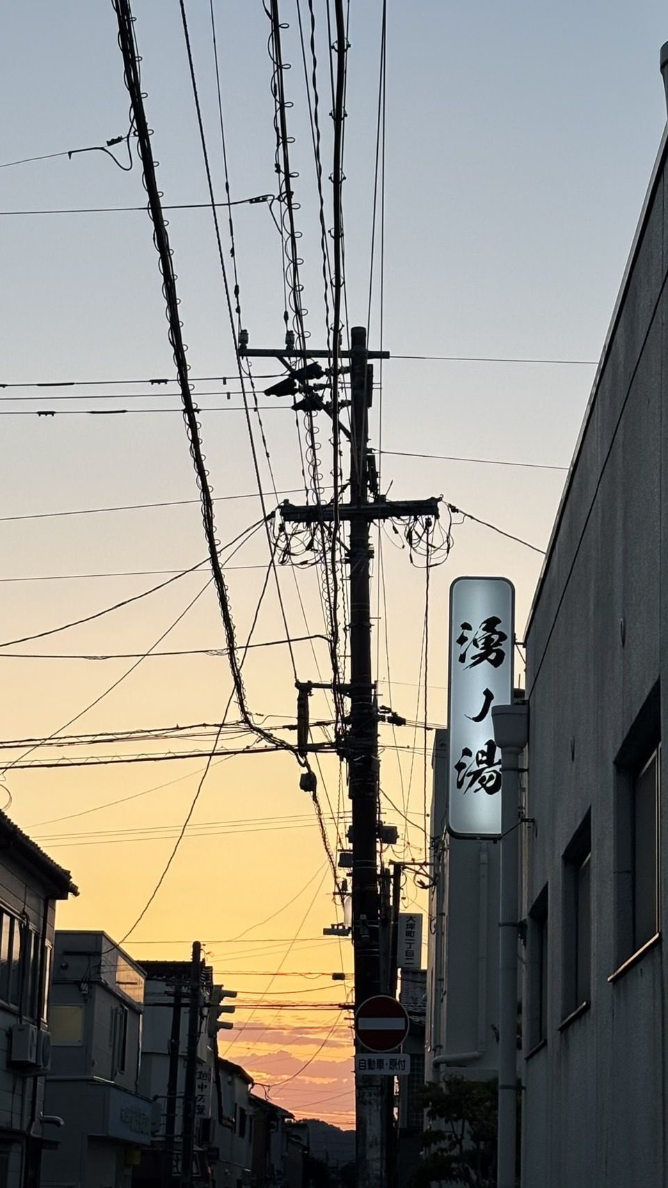 夕暮れの空と電線。灯りのともった湧ノ湯の袖看板